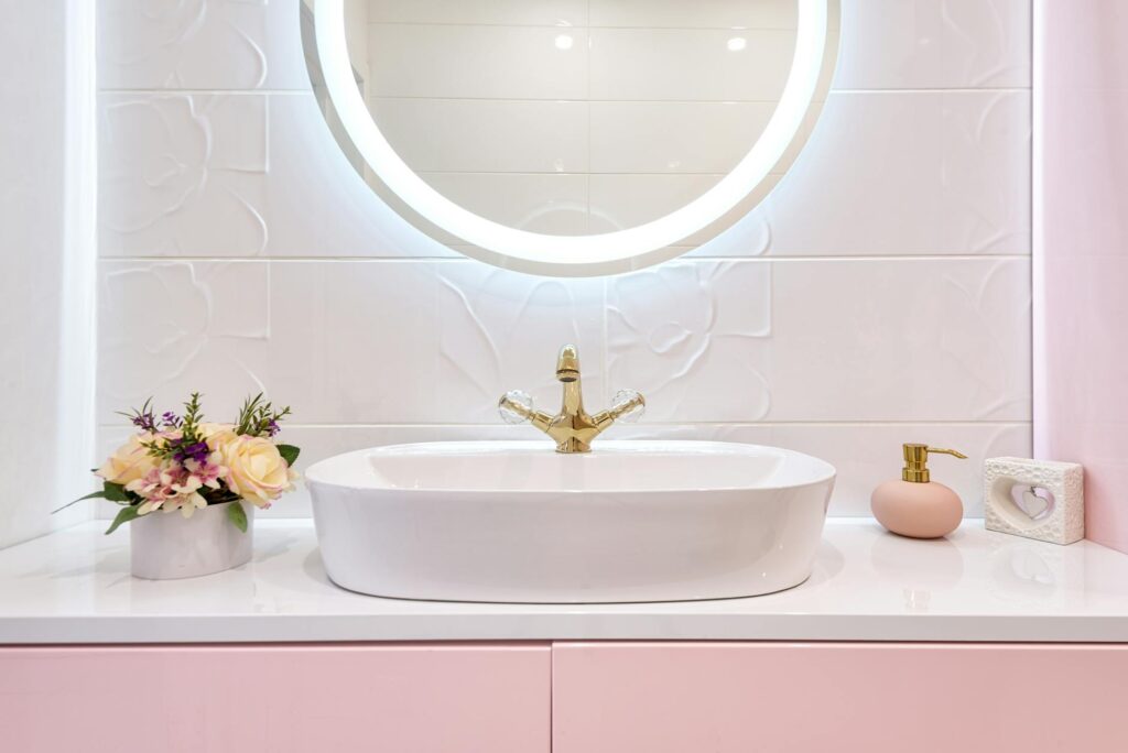 Interior of modern bathroom with luminous mirror hanging under sink with faucet near blooming flowers and soap